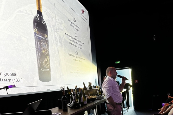 „Ein Sprecher erklärt die Weine vor der Leinwand, daneben stehen Flaschen und Gläser“