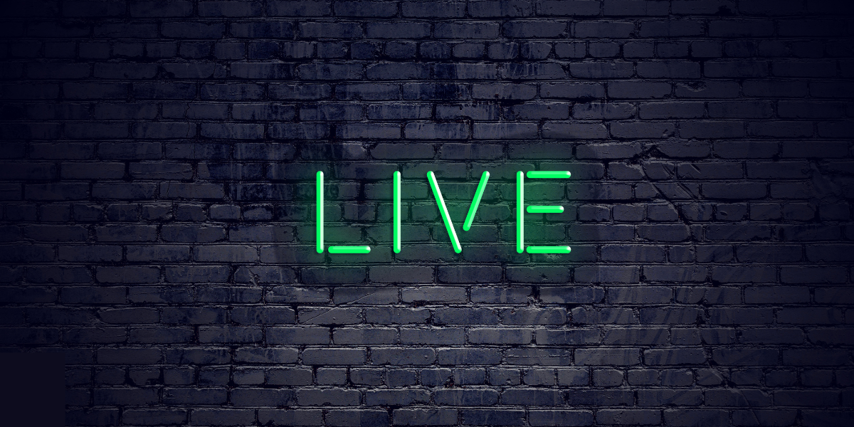 Foto, das eine schwarze Backsteinmauer zeigt, darauf angebracht ist ein neongrüner "LIVE"  Schriftzug, der leuchtet. 