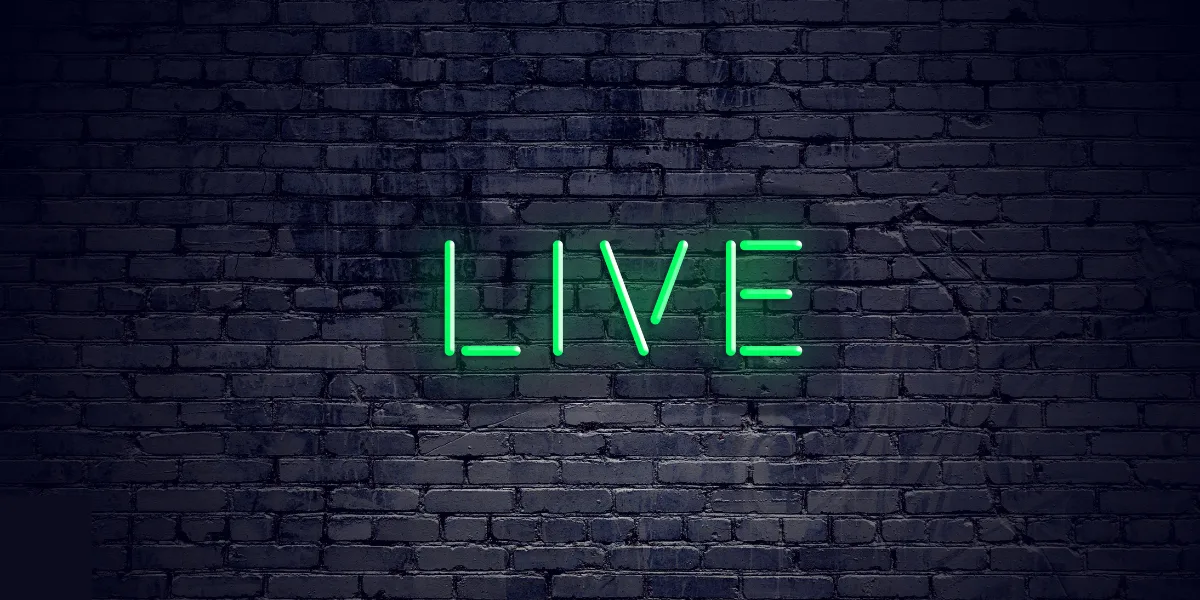 Foto, das eine schwarze Backsteinmauer zeigt, darauf angebracht ist ein neongrüner "LIVE" Schriftzug, der leuchtet.
