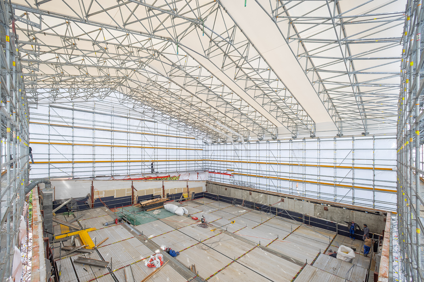 Innenansicht der Baustelle von Kino 5 des Dietrich Theater, vollständig von Gerüsten und weißen Planen umhüllt. Über dem Raum spannt sich eine hohe, gestützte Dachkonstruktion. Auf dem Boden liegen Baumaterialien und Werkzeuge.