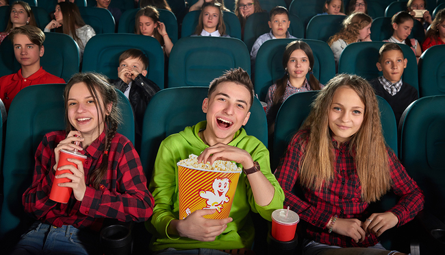 SchülerInnen mit Popcorn und Getränken sitzen in einem Kinosaal