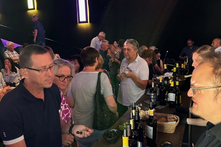„Besucher stehen am Weintisch, probieren verschiedene Weine und kommen ins Gespräch“