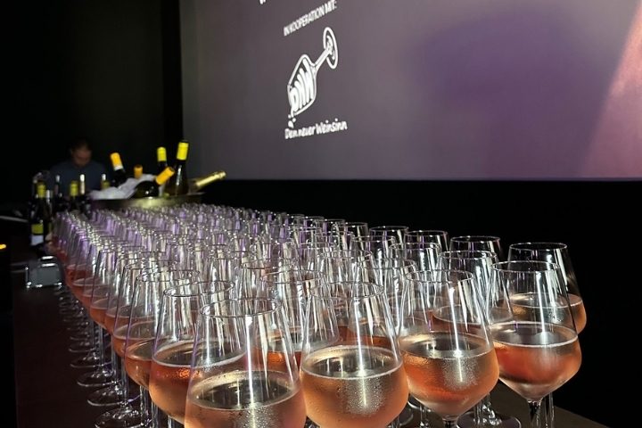 „Gefüllte Weingläser stehen bereit vor der Kinoleinwand für die Weinverkostung bei Kino et Vino“