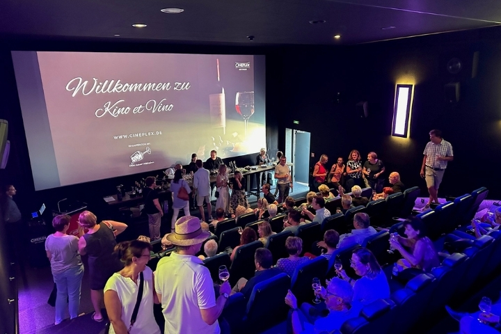 „Blick in den Kinosaal mit vielen Gästen, die sich vor der Leinwand mit Wein austauschen