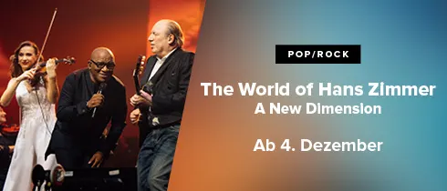 Hier sieht man Hans Zimemr mit zwei anderen Künstlern auf der Bühne, die musizieren.