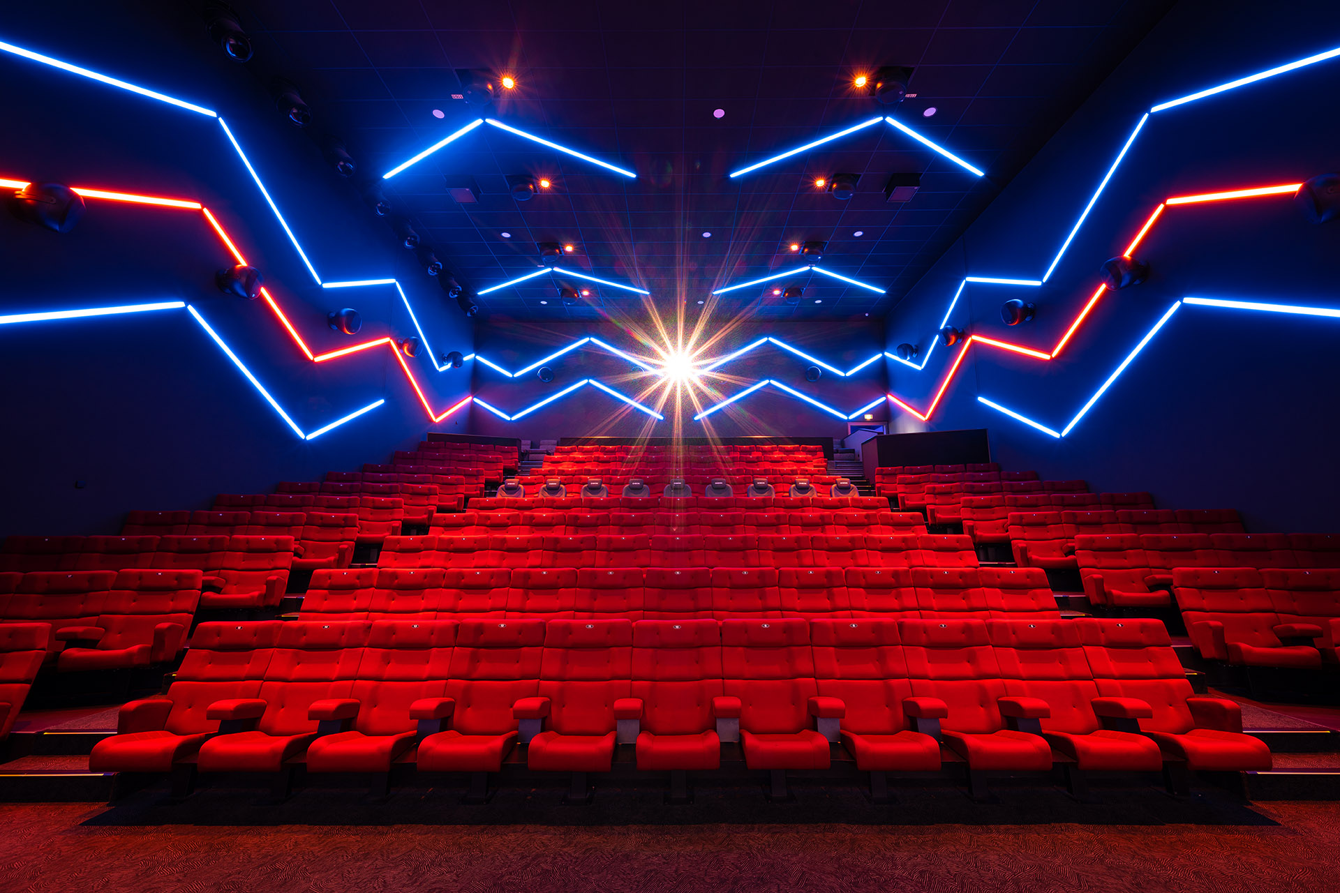 Foto, das den ULTIMATE. Saal mit roten Kinostühlen und blau-roter Beleuchtung des Cineplex Neufahrn zeigt