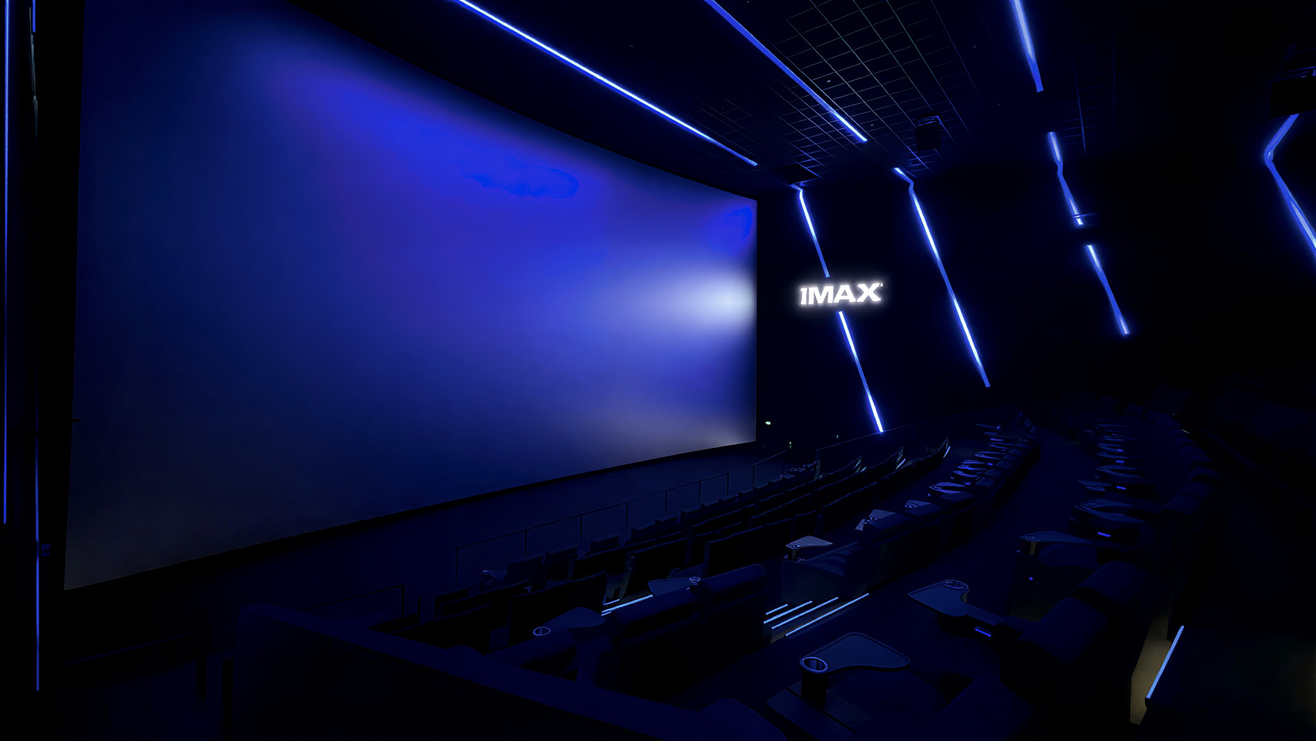 Dunkler IMAX-Kinosaal mit großer, leicht gebogener Leinwand, blauer LED-Beleuchtung an Wänden und Decke sowie sichtbaren Sitzreihen im Vordergrund.