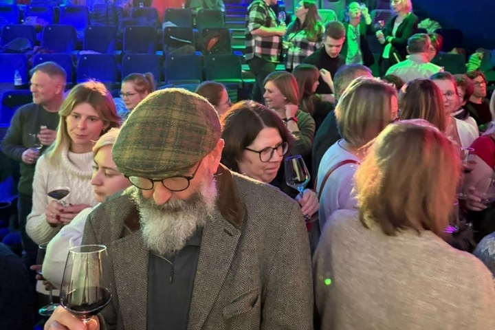 Besucherinnen und Besucher stehen im Kinosaal, unterhalten sich und probieren Wein während der Veranstaltung“