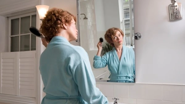 Женщина с кудрявыми волосами расчёсывает волосы