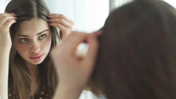 Девушка изучает свои волосы в зеркале