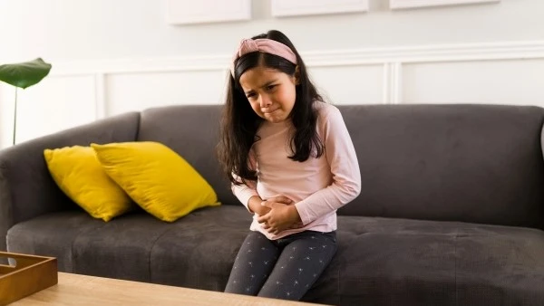 Боль в животе — один из симптомов болезни Крона у детей Девочка держится за живот и ощущает боль при болезни Крона