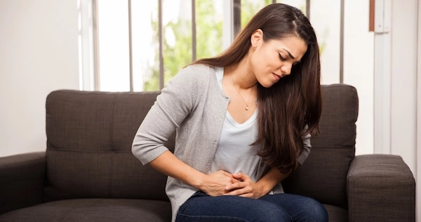 Девушка сидит на диване и держится за живот