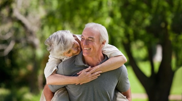 Пожилой мужчина с пожилой женщиной на спине, они улыбаются
