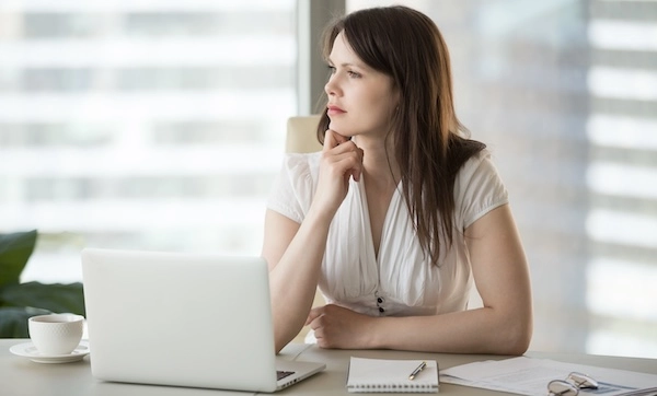 Женщина за компьютером задумчиво смотрит вдаль