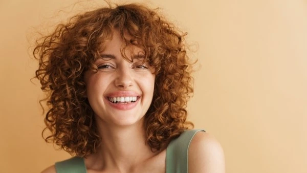 Девушка с кудрявыми рыжими волосами улыбается