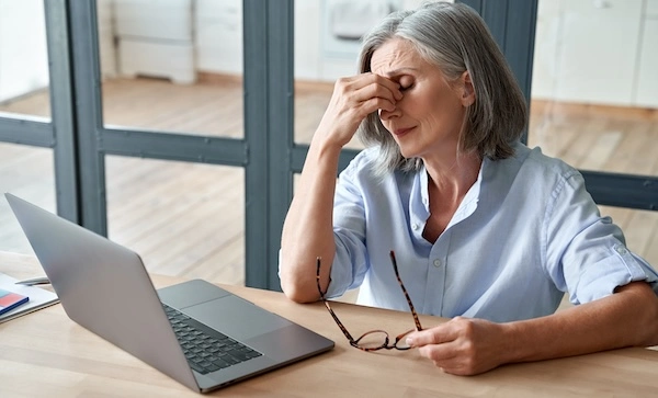 Пожилая женщина держится рукой за переносицу