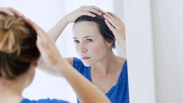Девушка смотрит на свои волосы в зеркале