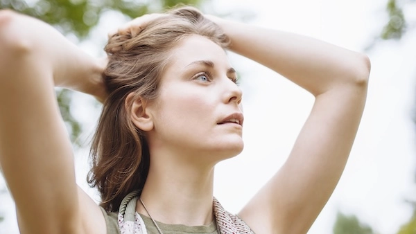 Девушка держится обеими руками за затылок Девушка держит руки на затылке