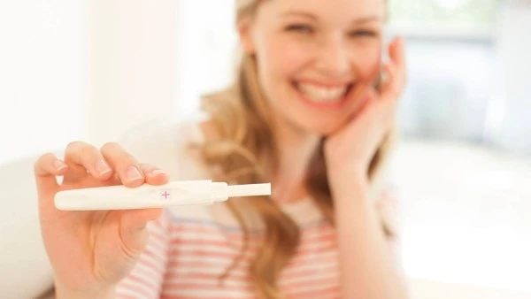 Одна из причин запоров в первом триместре — повышенная продукция прогестерона Счастливая девушка показывает положительный тест на беременность