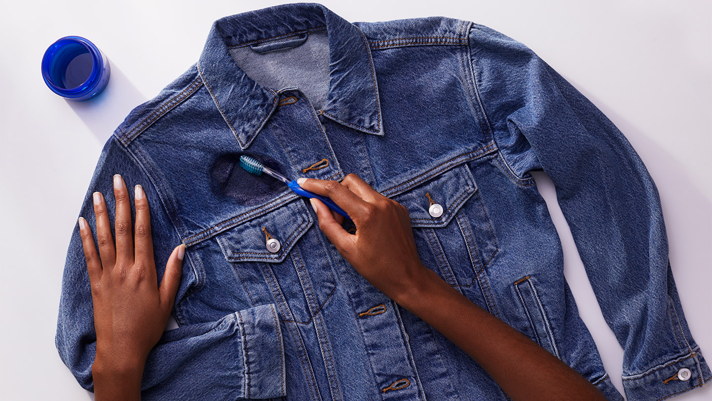 A person pretreating a denim jacket with Tide liquid laundry detergent and a toothbrush