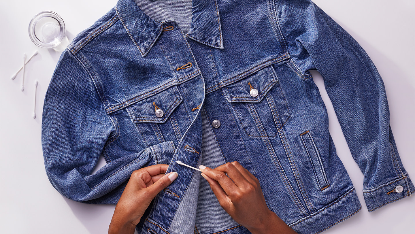 A person removing excess stain from a denim jacket with a cotton swab