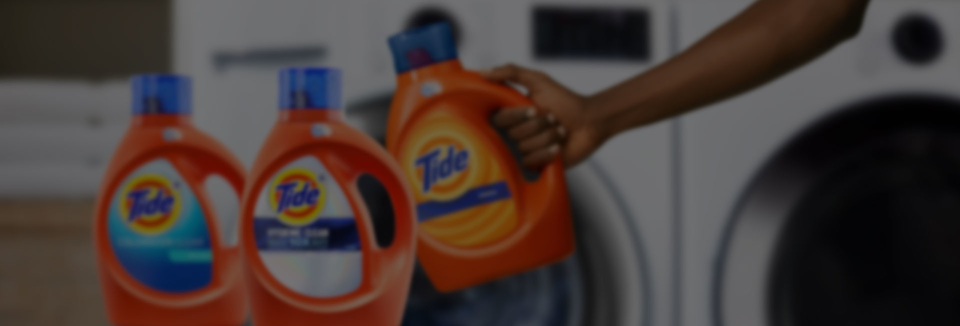 A person holding a Tide liquid detergent product in front of a washer