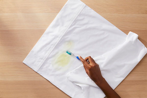 A person removing excess stain from a piece of white garment with a toothbrush
