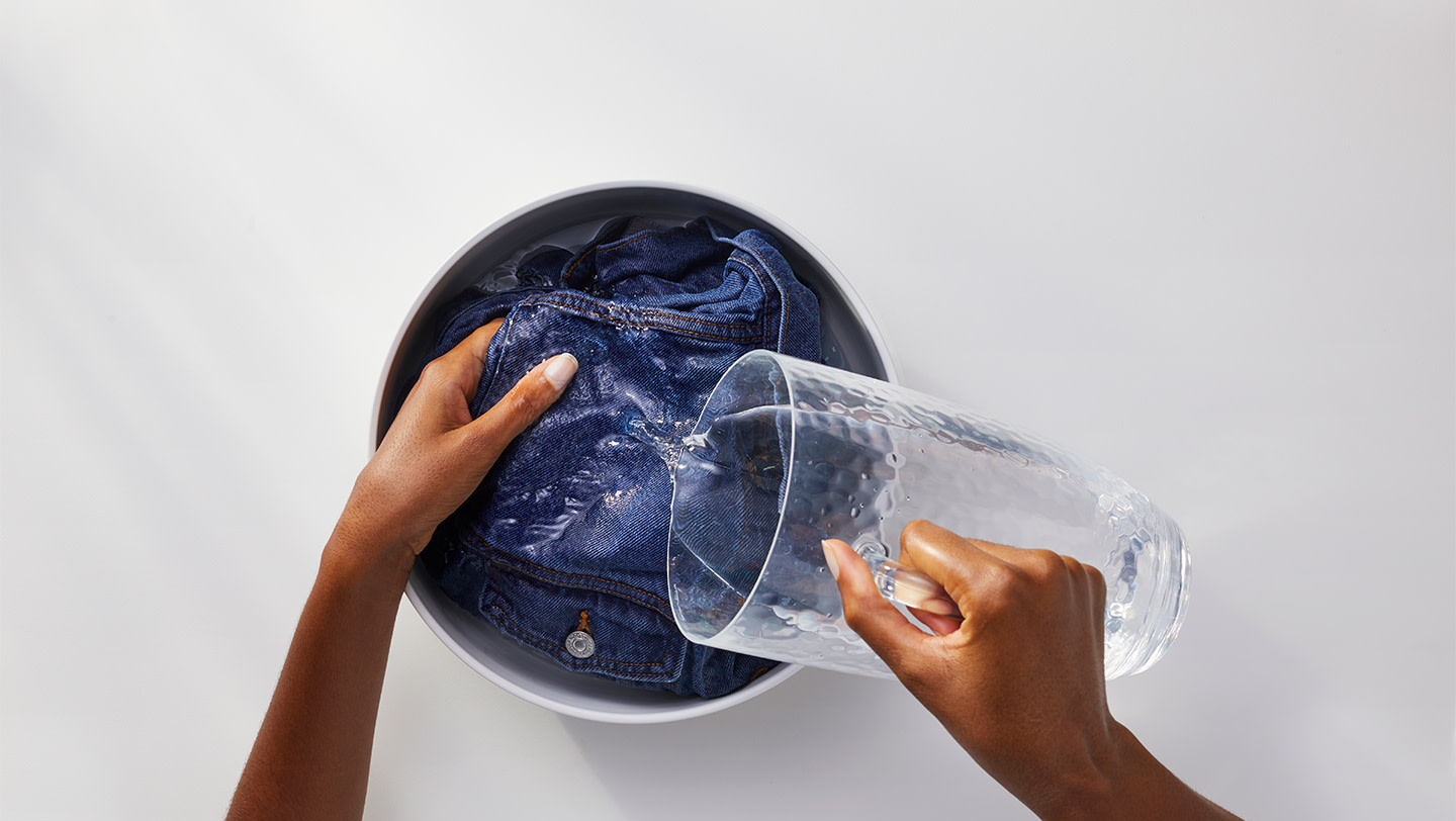 A person rinsing a denim jacket in cold water