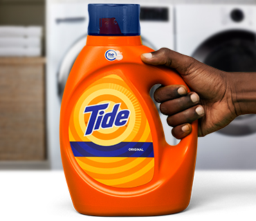 A person holding a Tide liquid detergent product in front of a washer