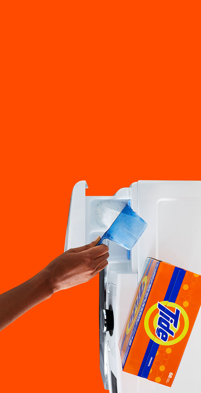 A person pouring Tide powder detergent into the detergent dispenser