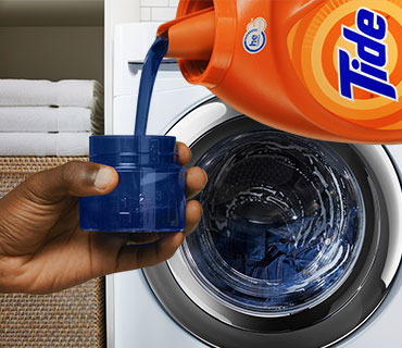 A person pouring Tide liquid detergent into a measurement cup