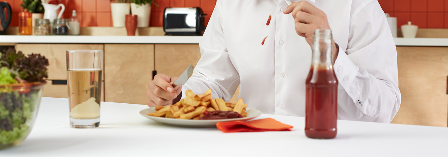 A person wearing a white shirt stained with ketchup