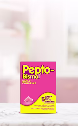Pink and yellow Pepto-Bismol Caplet box for 5-symptom relief, displayed on a white surface with a blurred background.