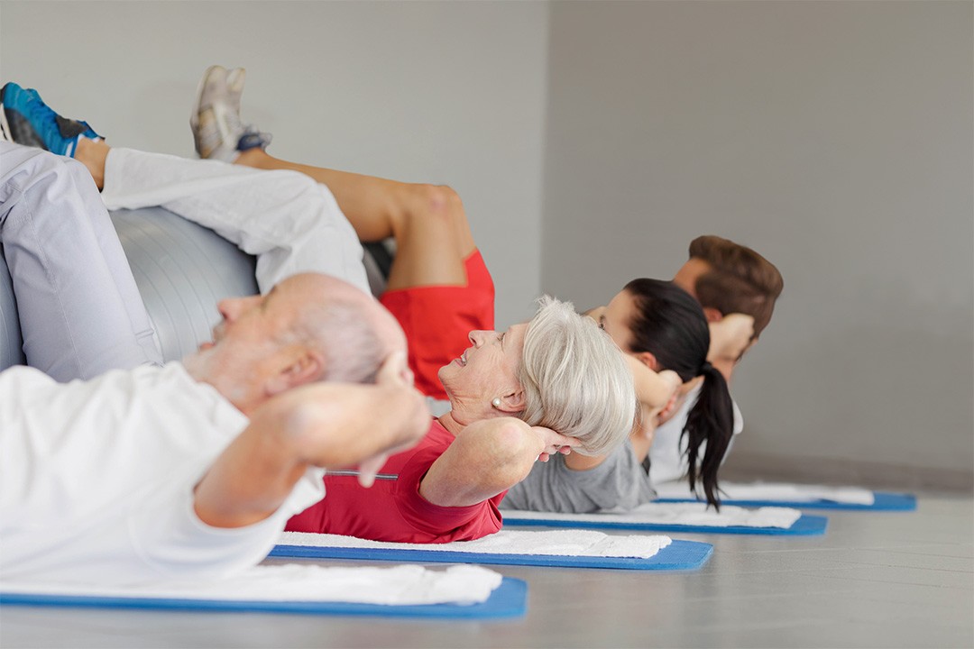 Vier Personen liegen auf einer Matte und machen eine Gymnastikübung.