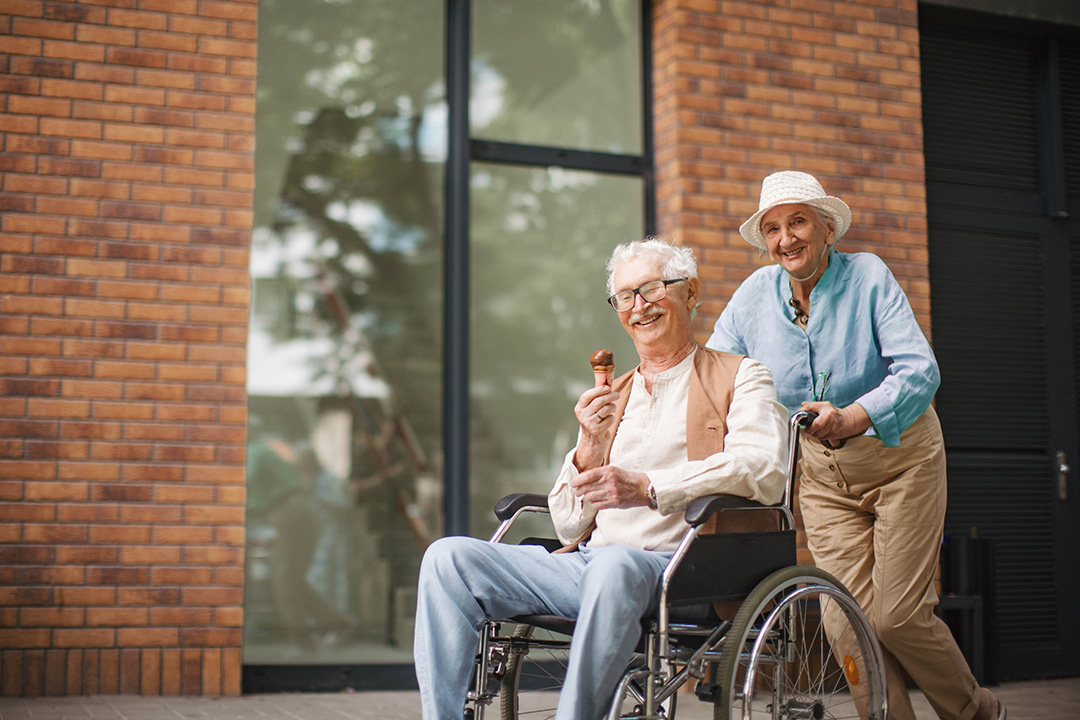 Eisessender Mann im Rollstuhl wird von Bekannten geschoben.