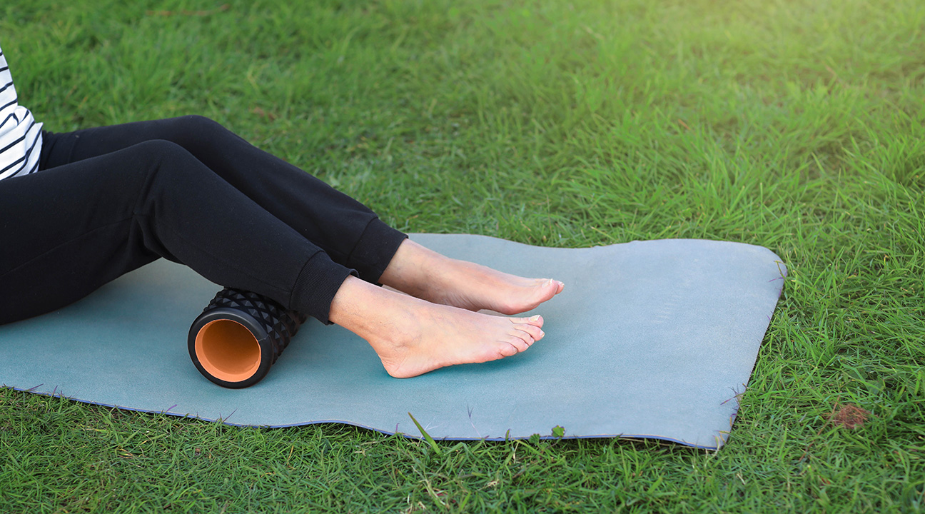 auf einer Wise liegende Person dehnt mit einer Faszienrolle die Waden aus.