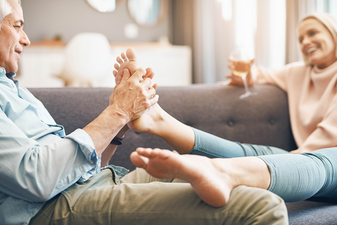 Mann massiert die Füße einer Frau auf den Sofa liegend.