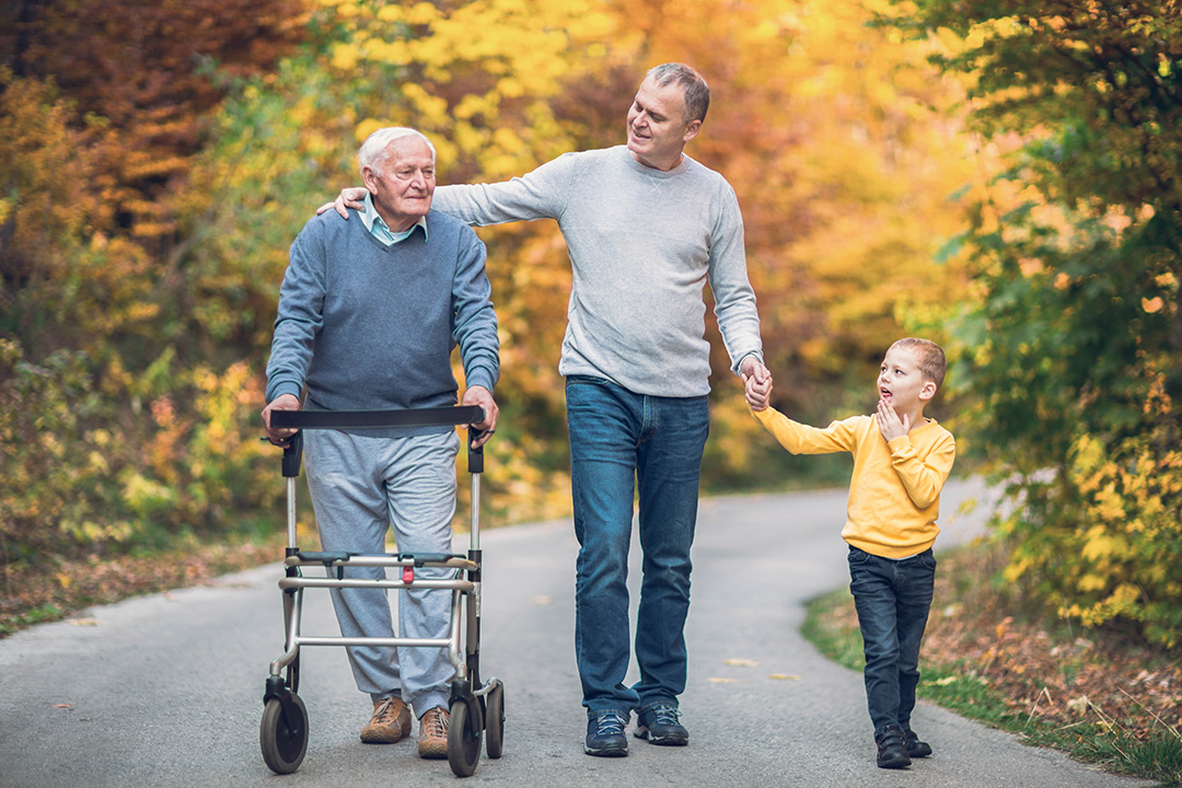 Ein Senior, ein Mann und ein Kind laufen zusammen einen Weg in der Natur.