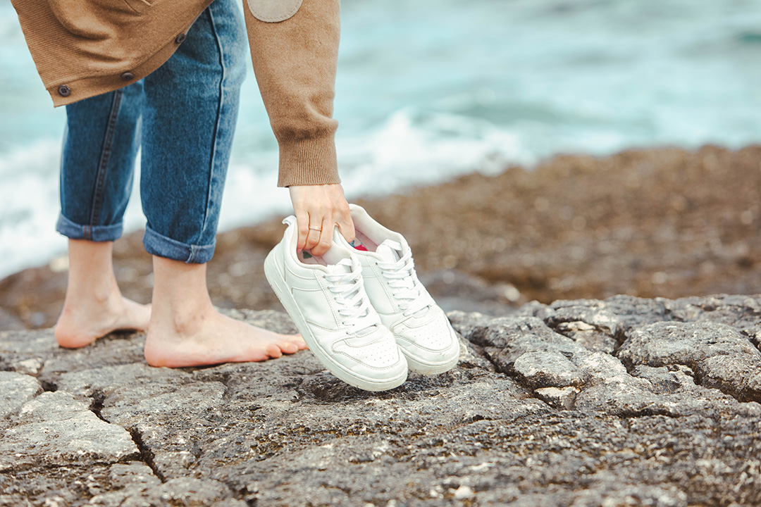 Frau hat ihre Sneaker ausgezogen und geht barfuß weiter.