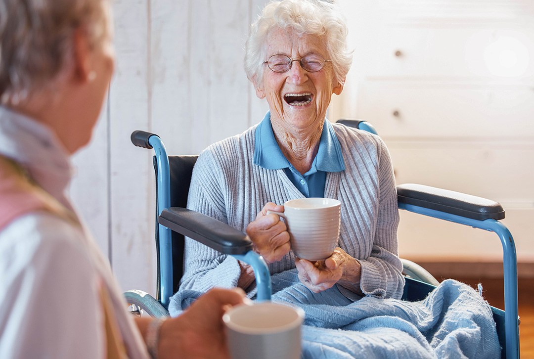 Eine im Rollstuh sitzende Seniorin lacht beherzt.
