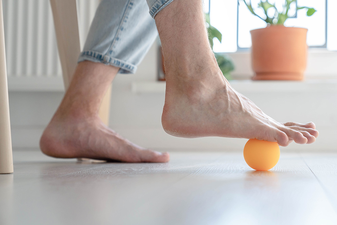 Person rollt sich mit Ball die Füße aus.