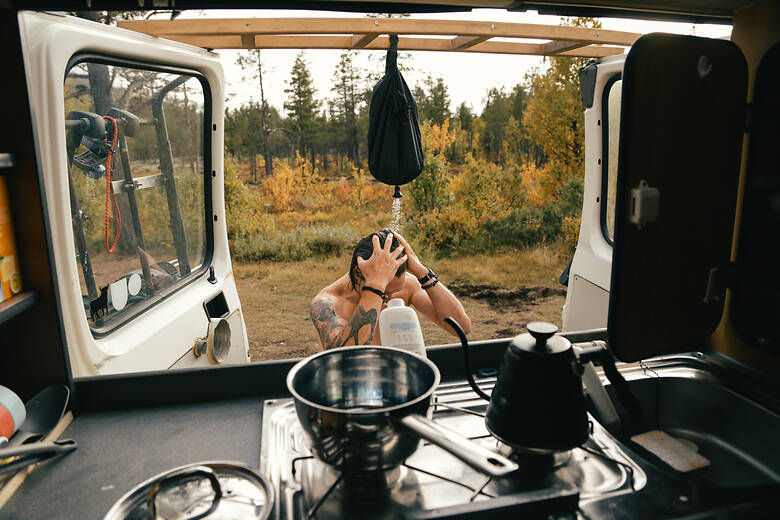 Mann duscht vor dem Camper in der Natur 