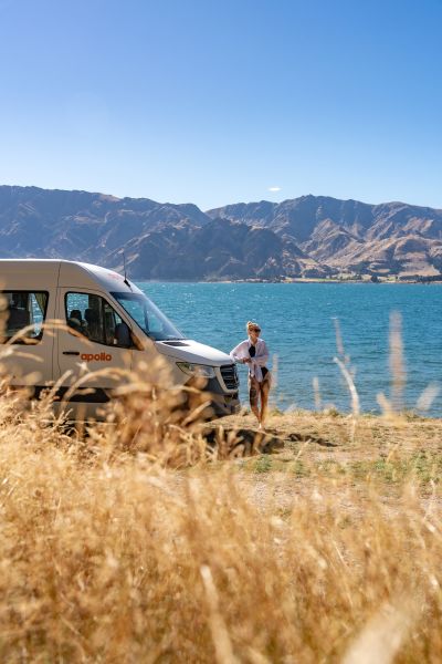 Frau lehnt an einem Camper in Neuseeland vor einem See