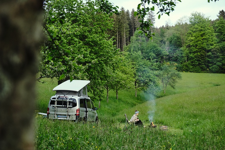 Frau campt auf einer großen grünen Wiese mit Camper