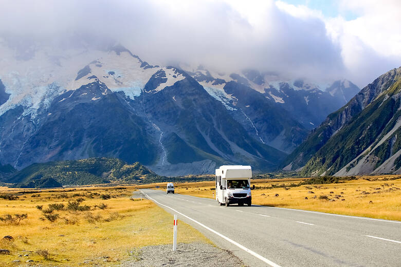 Wohnmobil fährt über eine Straße in Neuseeland, im Hintergrund sind schneebedeckte Berge zu sehen