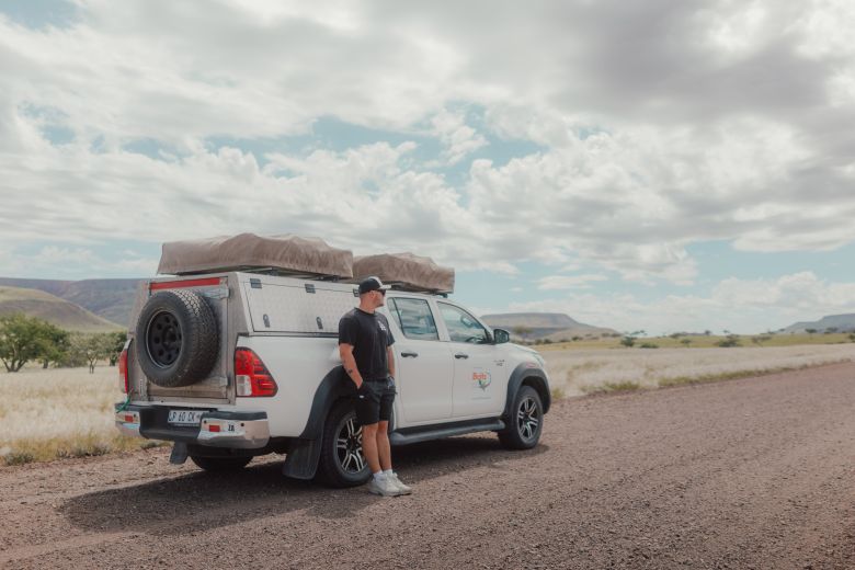 Mann lehnt lässig an einem Allrad-Camper in Namibia auf einer Schotterstraße
