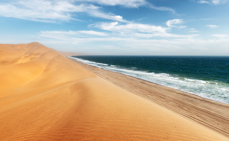 Atlantikwellen treffen auf Sanddünen in Namibia an der Skeleton Coast