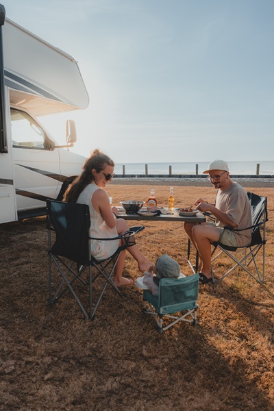 Familie mit Kind sitzt am Strand vorm Wohnmobil