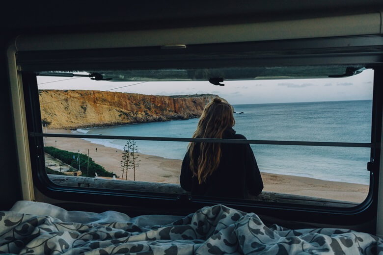 Frau sitzt im Camper und schaut auf das Meer in Portugal