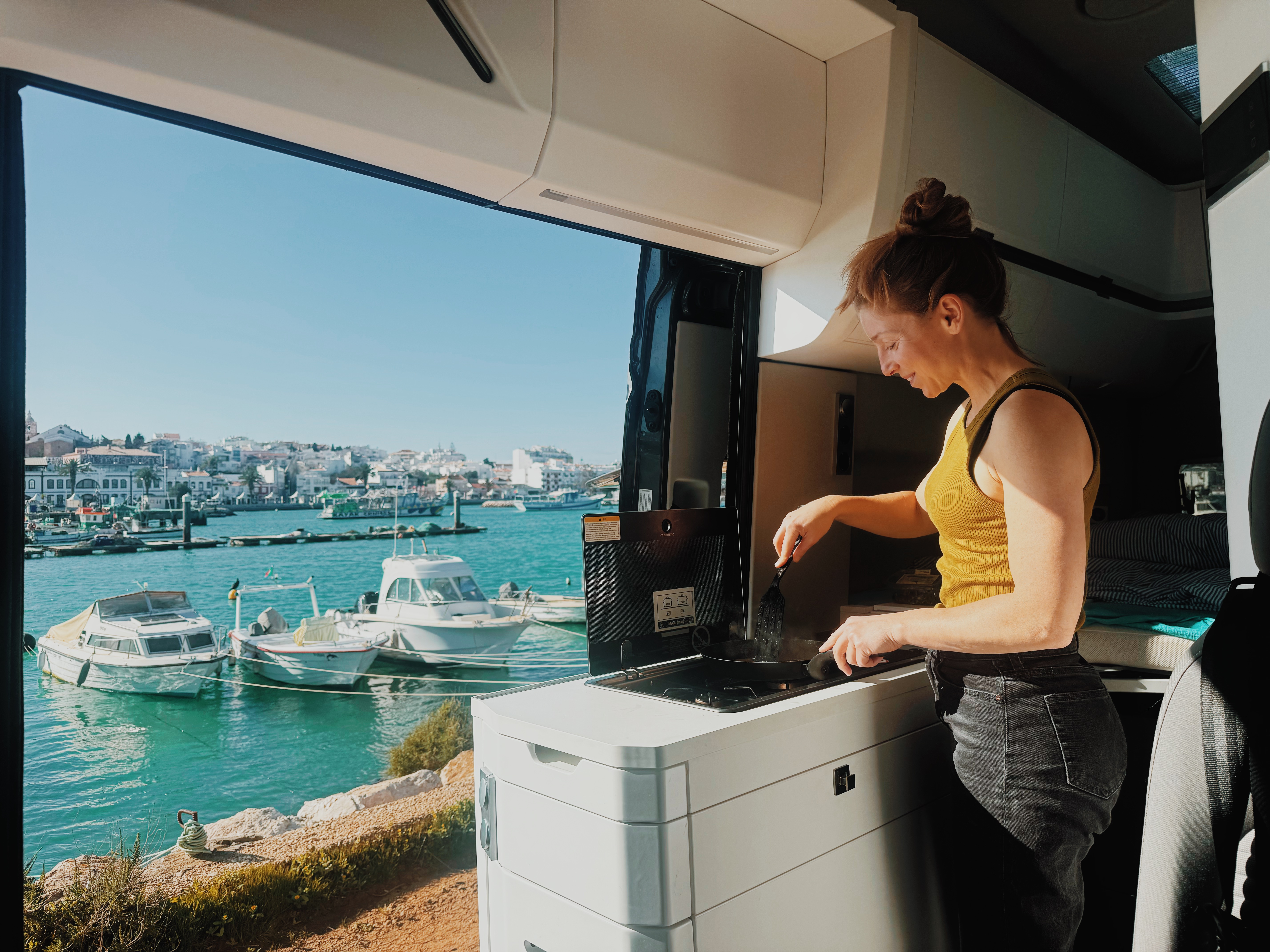 Frau kocht im Camper in Portugal mit Blick auf den Hafen